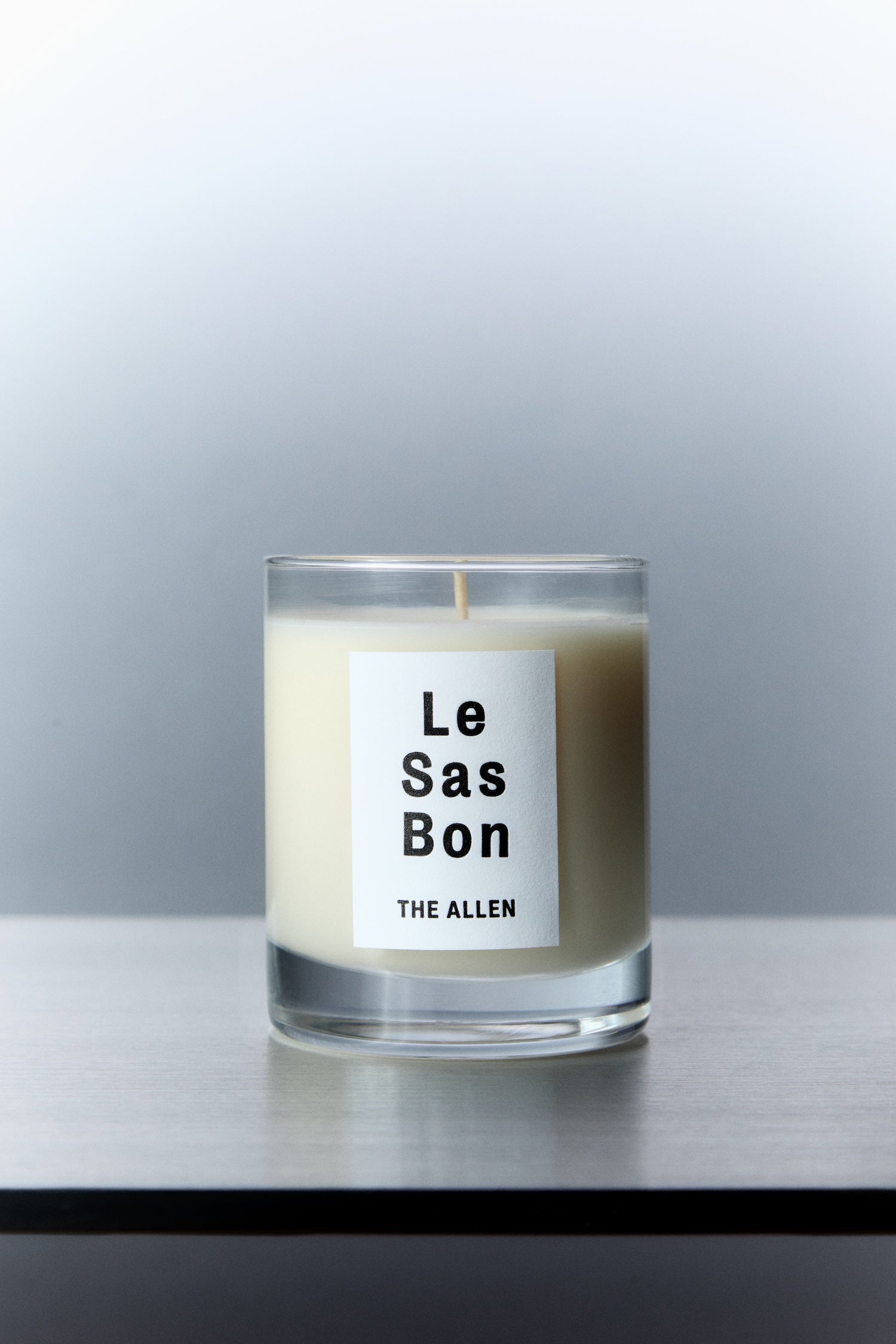Le Sas Bon "The Allen" eco-friendly candle in glass vessel with white rectangle branded sticker against a silver background