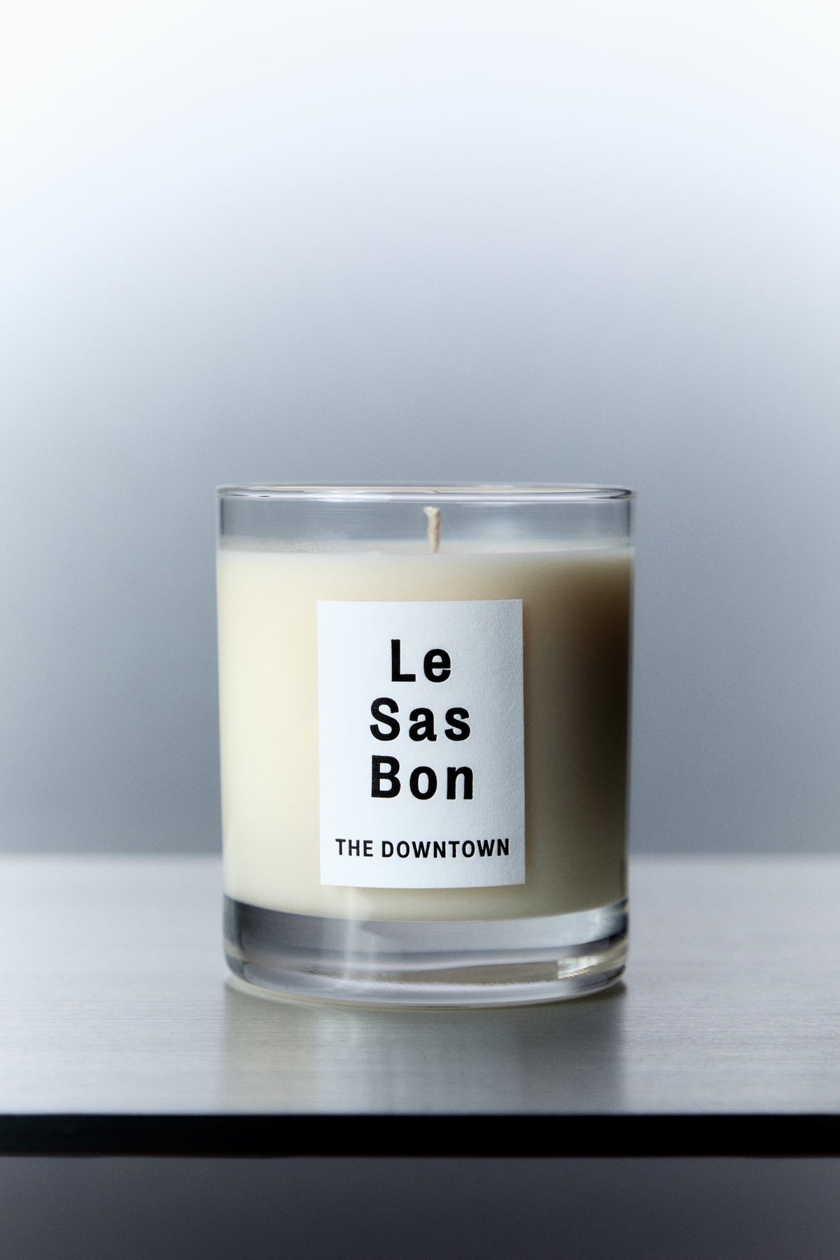Le Sas Bon "The Dowtown" natural candle in glass vessel with white rectangle branded sticker against a silver background