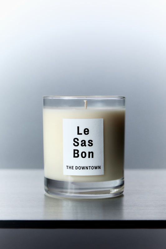 Le Sas Bon "The Dowtown" natural candle in glass vessel with white rectangle branded sticker against a silver background