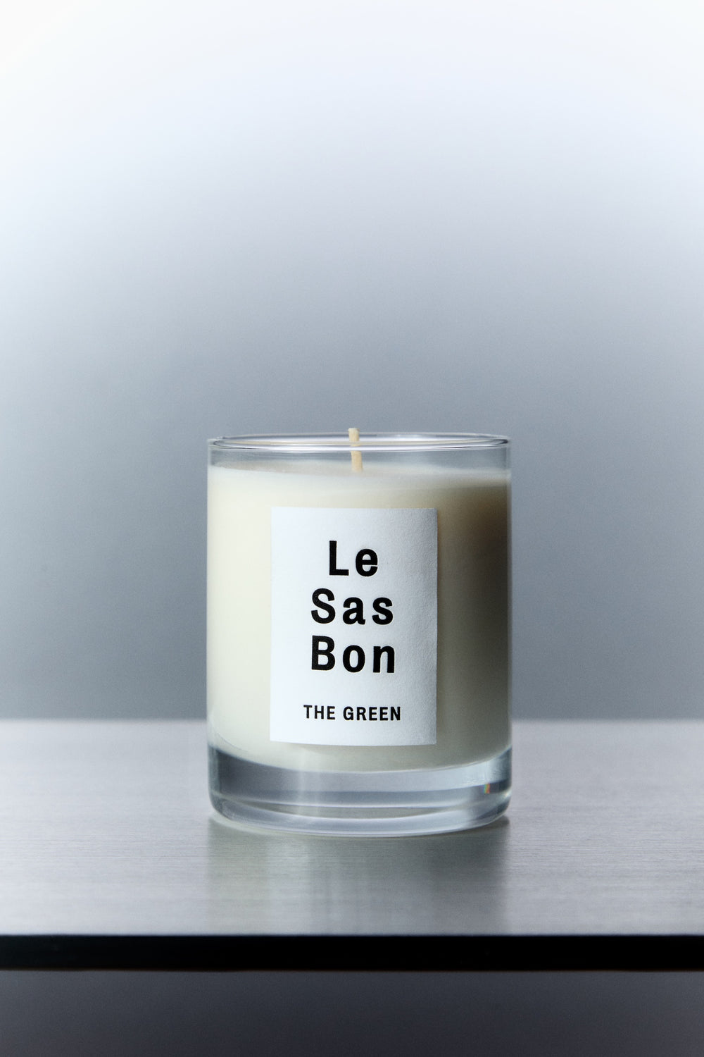 Le Sas Bon "The Green" natural candle in glass vessel with white rectangle branded sticker against a silver background