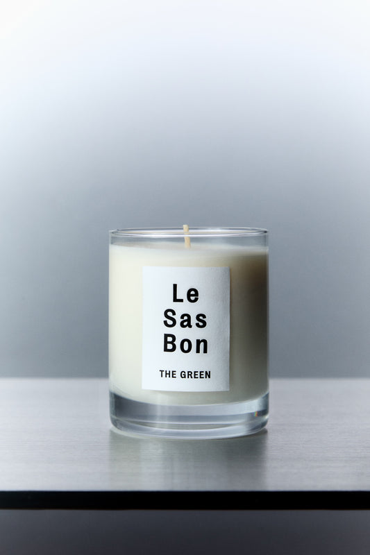 Le Sas Bon "The Green" natural candle in glass vessel with white rectangle branded sticker against a silver background