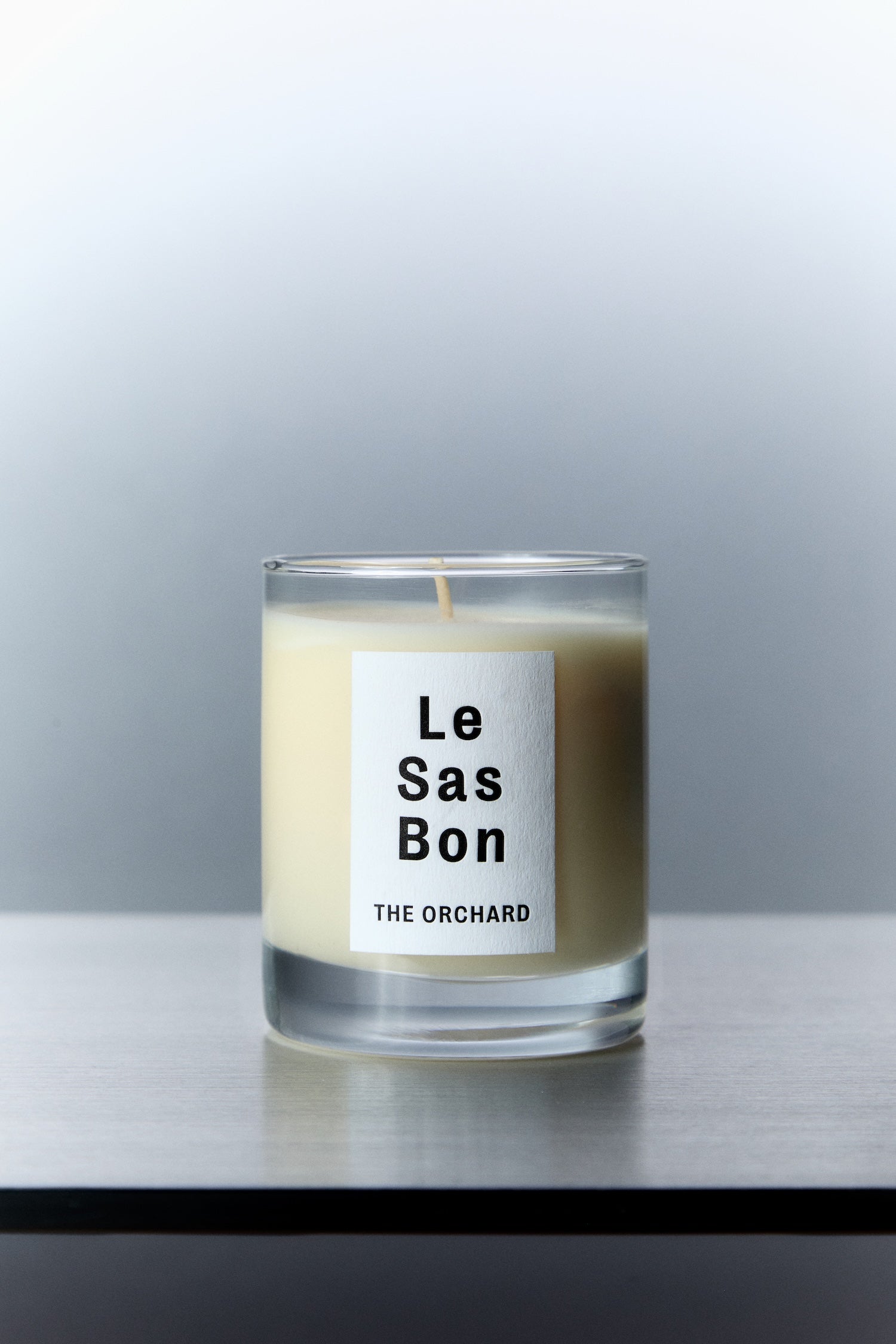 Le Sas Bon "The Orchard" organic and vegan candle in glass vessel with white rectangle branded sticker against a silver background