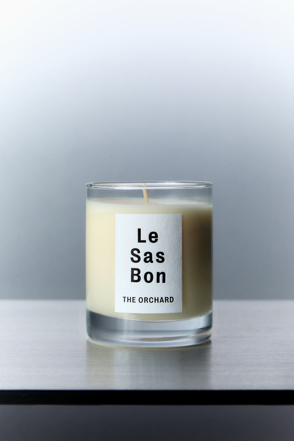 Le Sas Bon "The Orchard" organic and vegan candle in glass vessel with white rectangle branded sticker against a silver background