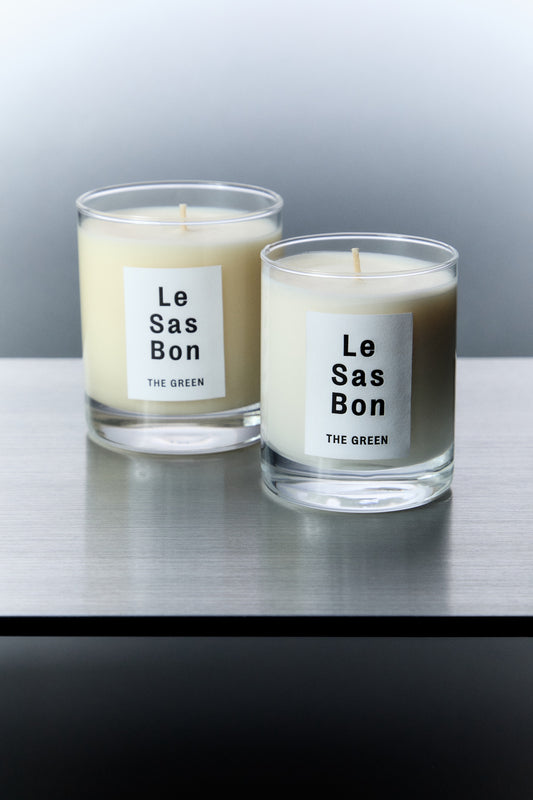 Le Sas Bon "The Green" natural candle in size 7.5oz and 10oz next to each other each in a glass vessel with white rectangle branded sticker against a silver background