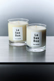 Le Sas Bon "The Green" natural candle in size 7.5oz and 10oz next to each other each in a glass vessel with white rectangle branded sticker against a silver background